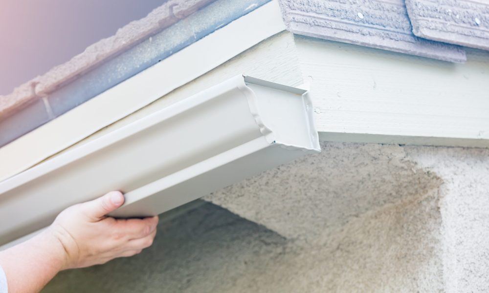 Worker Attaching Aluminum Rain Gutter to Fascia of House.